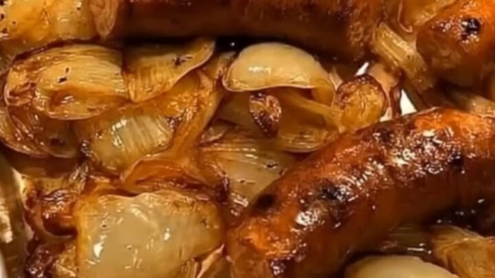 Browned roasted sausages on a bed of glossy caramelized onions on a white plate, steam rising