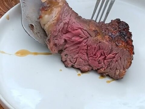 Seared tomahawk ribeye with a dark charred crust resting on a wooden cutting board, a thick slice showing a rosy pink center