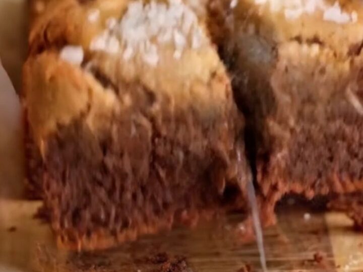 A stack of brown butter brookies with a fudgy brownie layer and chewy cookie layer, topped with flaky sea salt.