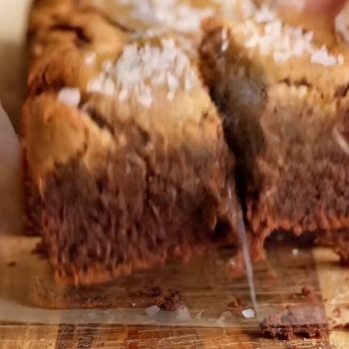 A stack of brown butter brookies with a fudgy brownie layer and chewy cookie layer, topped with flaky sea salt.