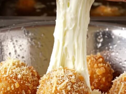 Golden fried potato cheese balls with a mozzarella pull on a rustic plate