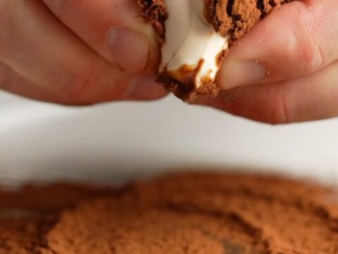 A cocoa-dusted tiramisu truffle broken in half, revealing a creamy espresso mascarpone center.