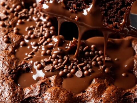 A fork lifting a slice of Turkish wet chocolate cake, showing the glossy fudge sauce and crispy chocolate pearls.