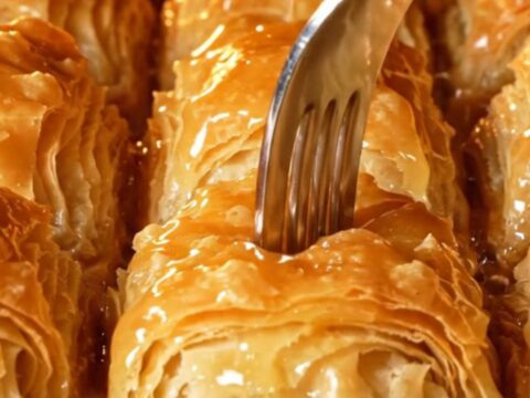 Golden mussel-shaped baklava with lemon syrup being poured over