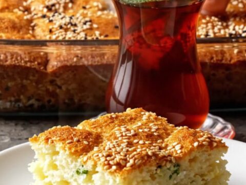 Golden square of Turkish sheet-pan cake with feta and herbs, lifted with a spatula, steam rising