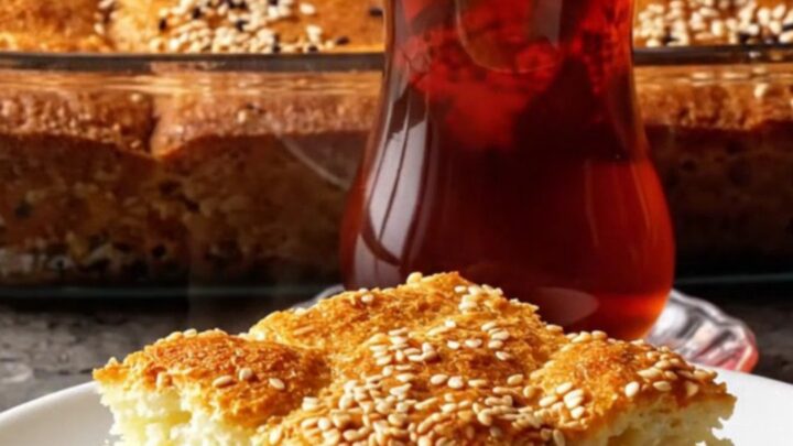Golden square of Turkish sheet-pan cake with feta and herbs, lifted with a spatula, steam rising