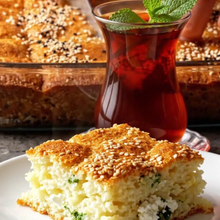 Golden square of Turkish sheet-pan cake with feta and herbs, lifted with a spatula, steam rising