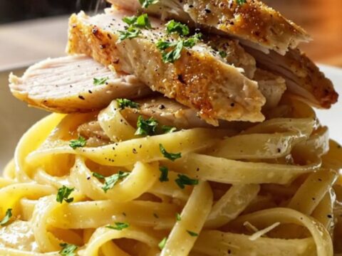 A fork twirling glossy lemon garlic fettuccine with sliced golden chicken breast, steam rising, garnished with parsley.