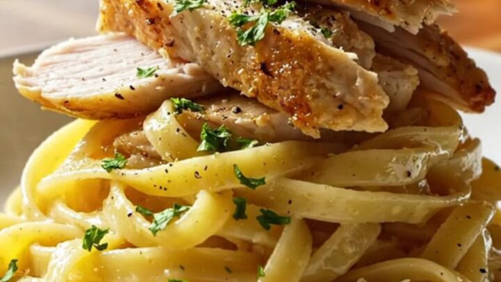 A fork twirling glossy lemon garlic fettuccine with sliced golden chicken breast, steam rising, garnished with parsley.