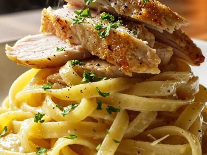 A fork twirling glossy lemon garlic fettuccine with sliced golden chicken breast, steam rising, garnished with parsley.