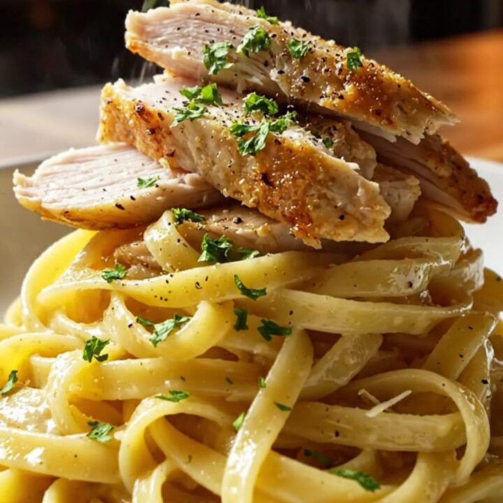 A fork twirling glossy lemon garlic fettuccine with sliced golden chicken breast, steam rising, garnished with parsley.
