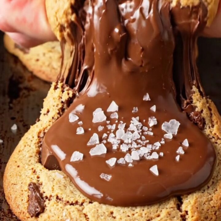 Two-chip bakery cookies stacked on a wire rack, showing crispy golden edges and gooey chocolate centers with flaky sea salt.