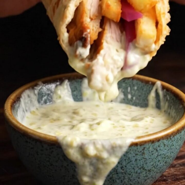 Crispy chicken shawarma wrap cut in half, showing layers of spiced chicken, garlic sauce, and pickles.