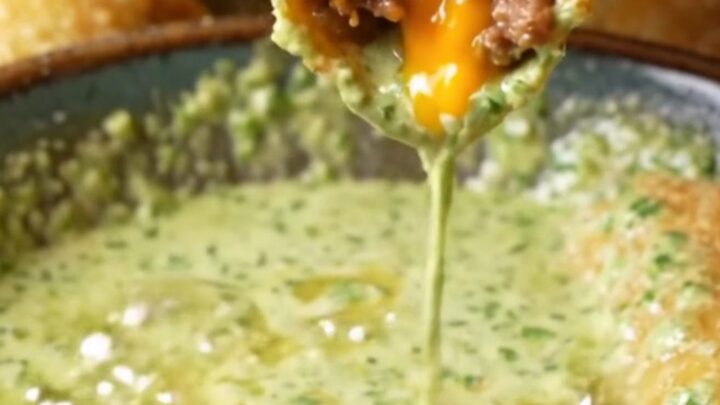 Golden crispy beef taquitos stacked on a plate with a bowl of cilantro lime crema for dipping.