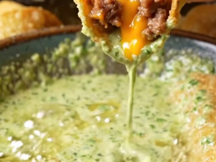 Golden crispy beef taquitos stacked on a plate with a bowl of cilantro lime crema for dipping.