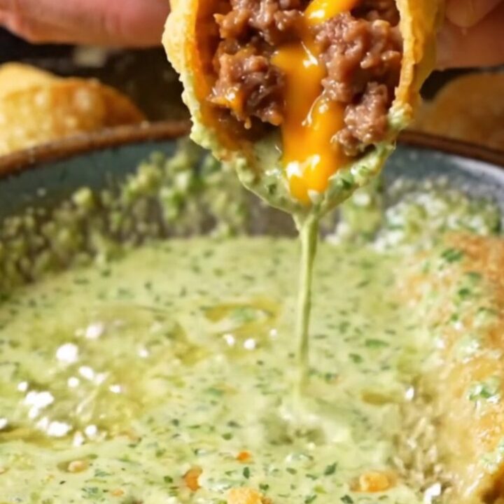 Golden crispy beef taquitos stacked on a plate with a bowl of cilantro lime crema for dipping.