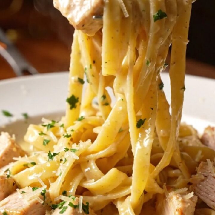 Creamy garlic parmesan chicken pasta in a skillet with a fork twirling fettuccine, topped with chicken and parsley.
