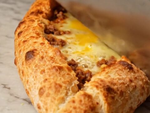 Sliced Turkish boat pide with spiced meat and melted cheese on a baking sheet