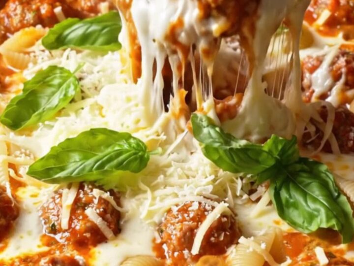 One-pot skillet with pasta shells, meatballs, and melted cheese, garnished with basil