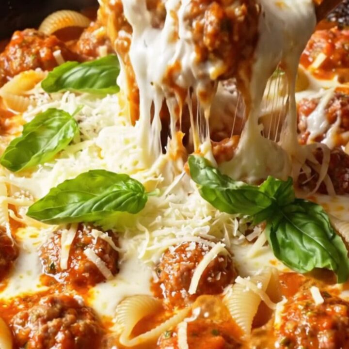 One-pot skillet with pasta shells, meatballs, and melted cheese, garnished with basil