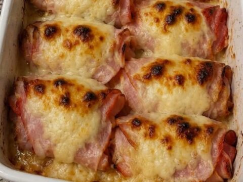 Huit rouleaux de jambon au fromage dorés et bouillonnants dans un plat blanc, une vapeur épaisse s'élevant au-dessus