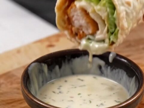 Golden toasted chicken Caesar wrap sliced diagonally on a cutting board, with creamy dressing visible inside.