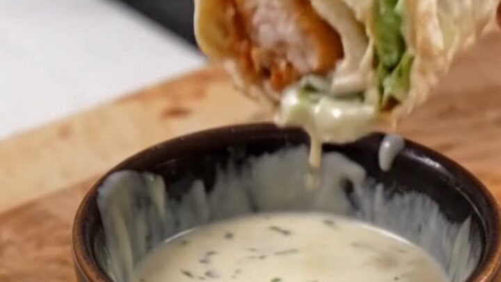 Golden toasted chicken Caesar wrap sliced diagonally on a cutting board, with creamy dressing visible inside.