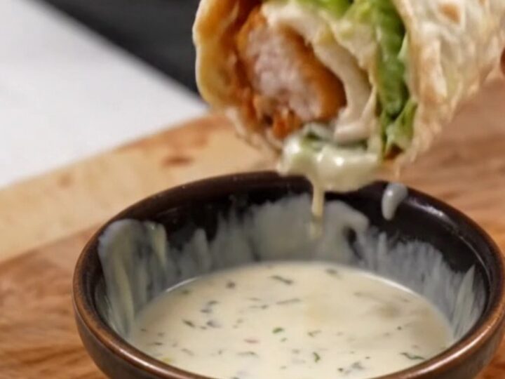 Golden toasted chicken Caesar wrap sliced diagonally on a cutting board, with creamy dressing visible inside.