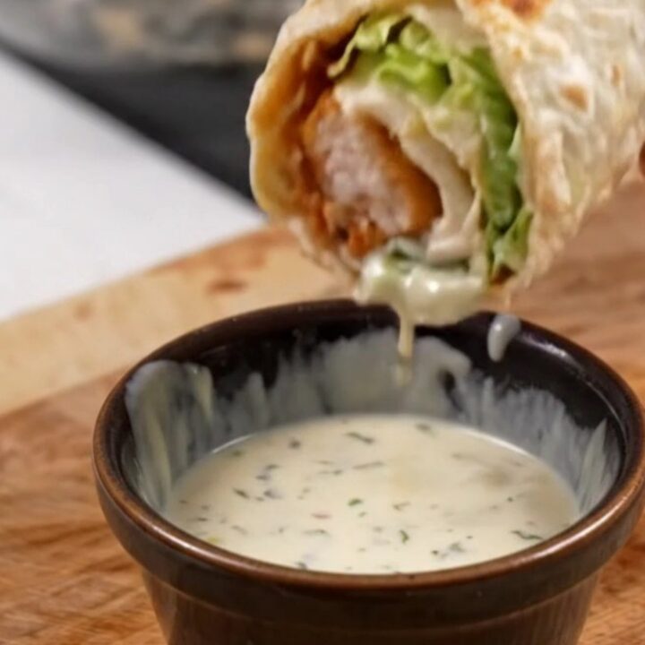 Golden toasted chicken Caesar wrap sliced diagonally on a cutting board, with creamy dressing visible inside.