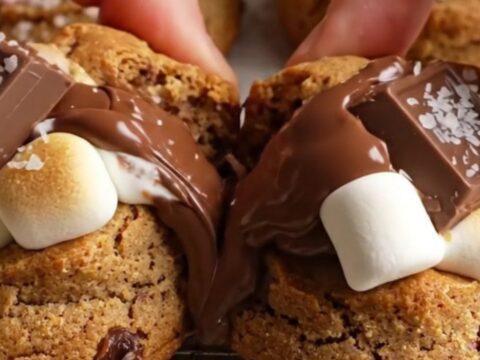 Warm s'mores cookies with gooey marshmallow pull and melted chocolate chunks on a parchment-lined baking sheet