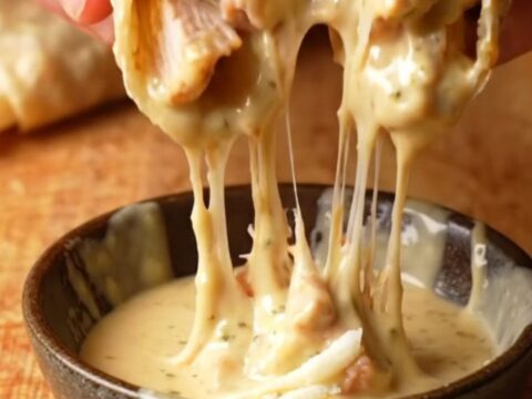 Crispy chicken alfredo wrap sliced in half with creamy sauce oozing out, golden tortilla