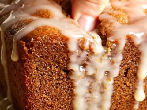 Golden whole-lemon walnut loaf cake with glossy lemon glaze, sliced on a wooden board.