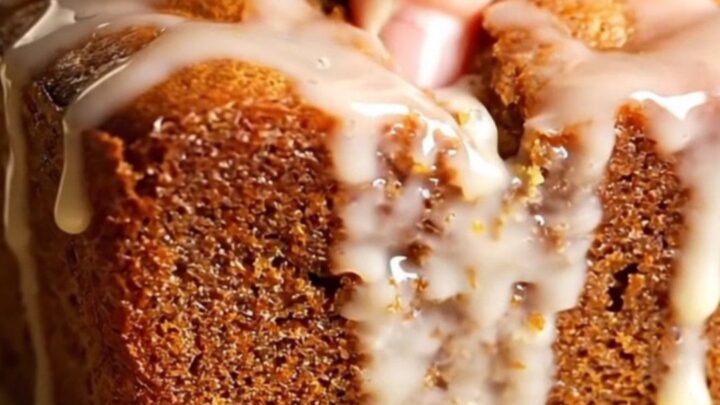 Golden whole-lemon walnut loaf cake with glossy lemon glaze, sliced on a wooden board.