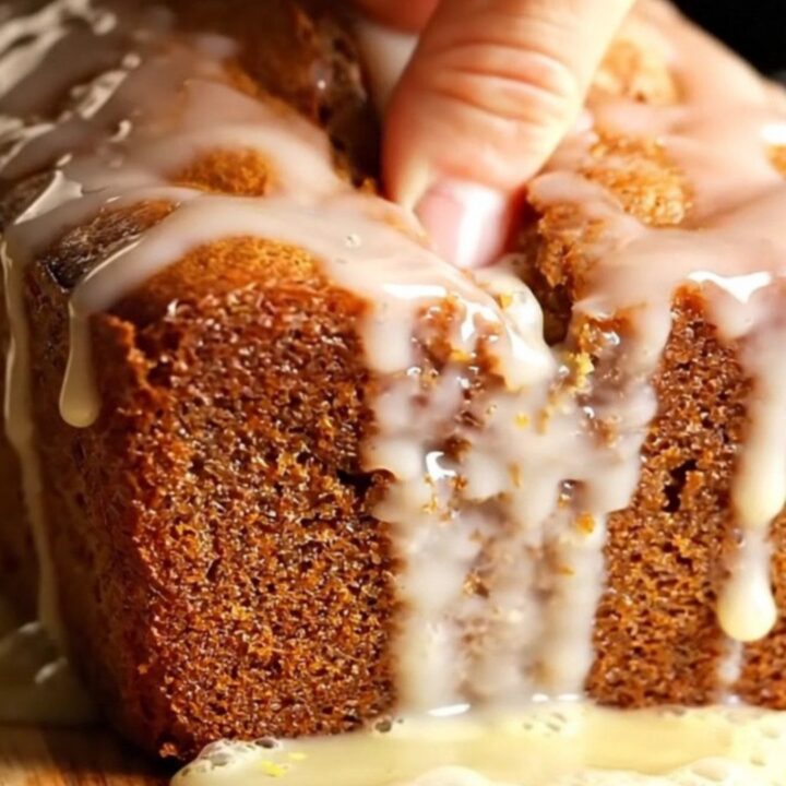 Golden whole-lemon walnut loaf cake with glossy lemon glaze, sliced on a wooden board.