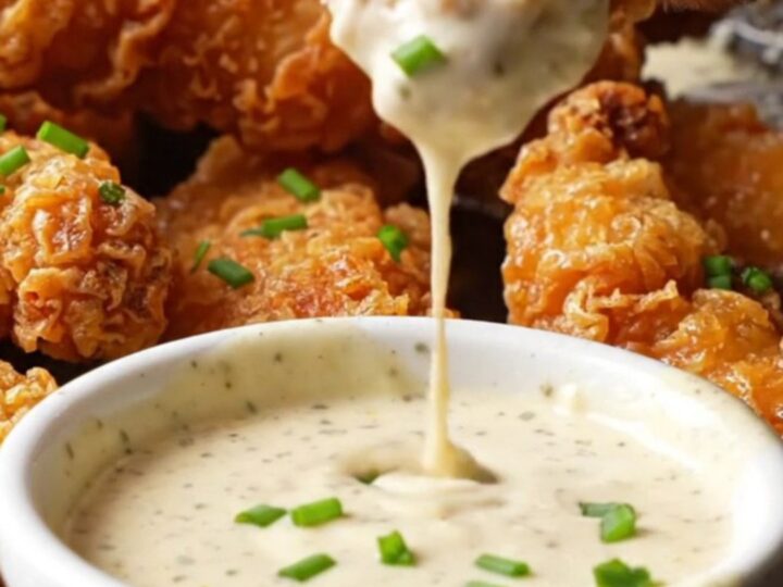 Golden crispy chicken tenders stacked on a wire rack, with a bowl of ranch for dipping