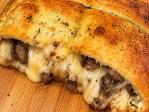 A warm, golden-brown loaf of stuffed bread on a wooden cutting board with steam rising from the center.