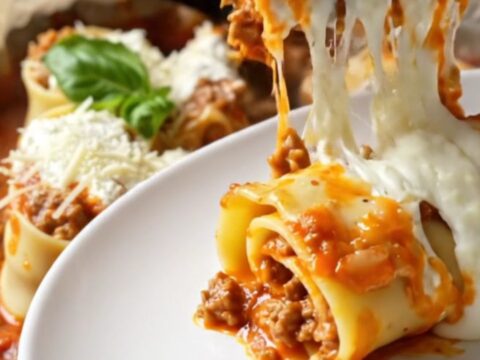 Skillet lasagna rollups with melted mozzarella and basil, lifted with a spatula