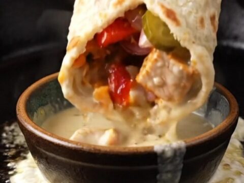A crispy chicken shish kebab wrap cut in half, showing charred chicken, sumac onions, and garlic sauce.