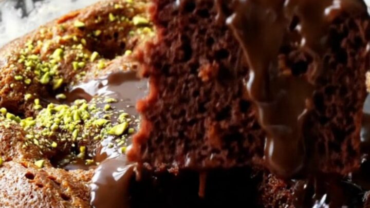 A fork lifting a slice of Turkish wet chocolate cake with fudge sauce oozing and pistachios on top