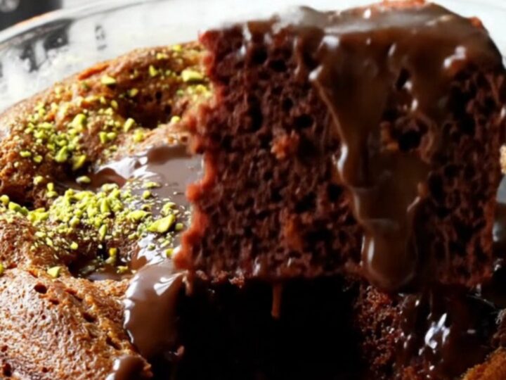 A fork lifting a slice of Turkish wet chocolate cake with fudge sauce oozing and pistachios on top