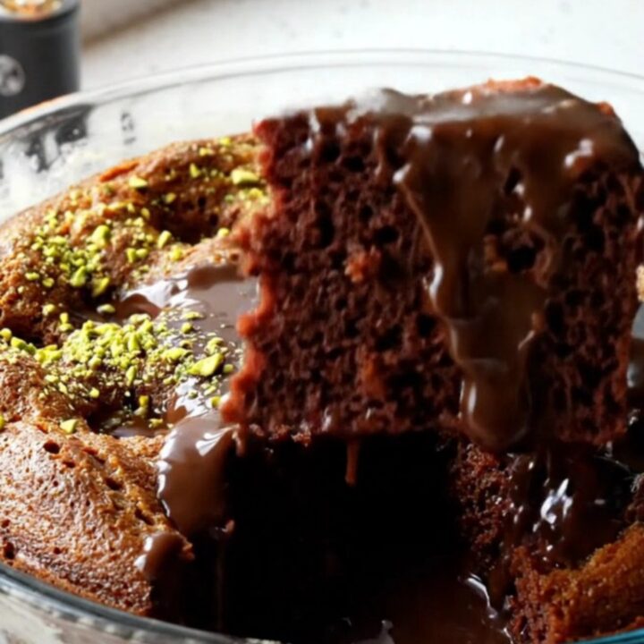 A fork lifting a slice of Turkish wet chocolate cake with fudge sauce oozing and pistachios on top