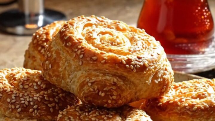 Golden crispy sesame cheese pinwheels on a parchment-lined baking sheet, showing flaky layers and melted feta.