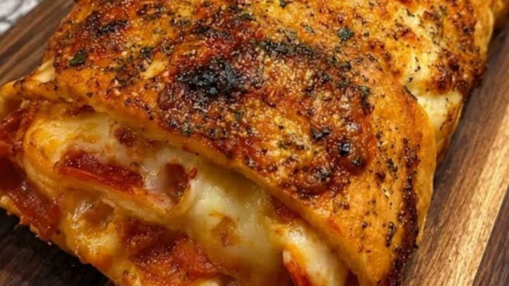 A beautifully browned, golden pepperoni stromboli garnished with fresh herbs on a dark wooden board.