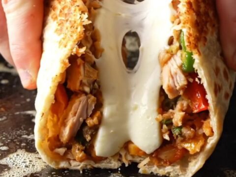 Crispy chicken Philly cheesesteak wrap cut in half with melted cheese stretching out