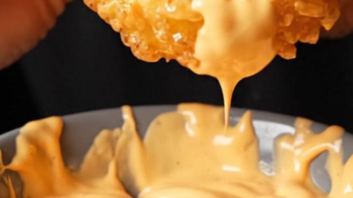 Golden crispy potato rings piled on a plate with a bowl of spicy mayo dip
