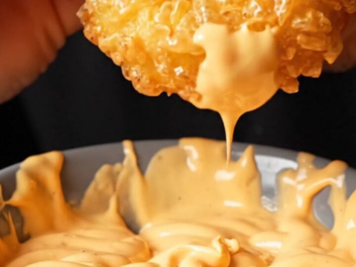 Golden crispy potato rings piled on a plate with a bowl of spicy mayo dip