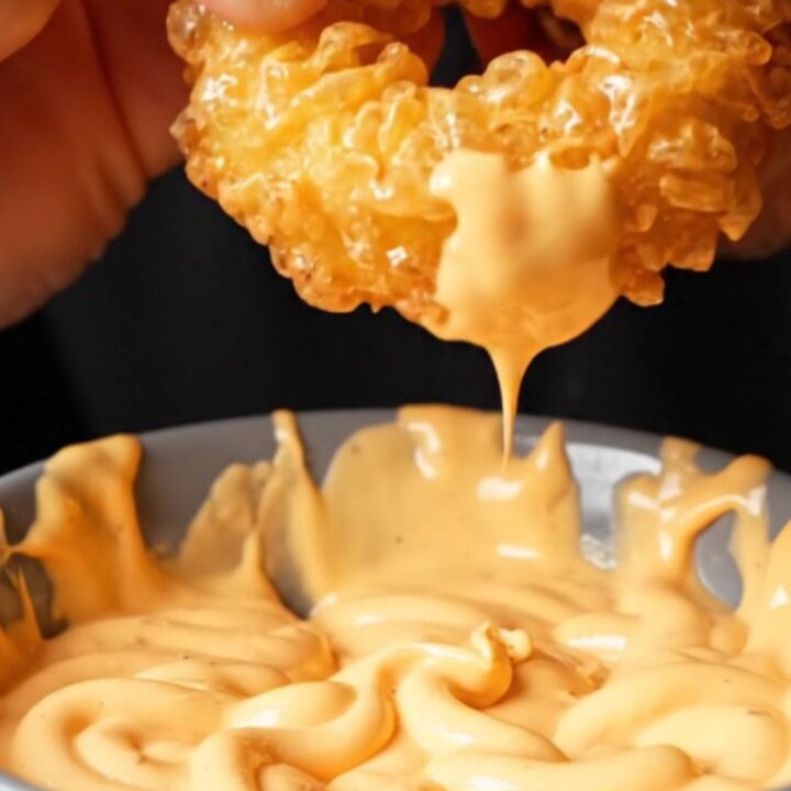 Golden crispy potato rings piled on a plate with a bowl of spicy mayo dip