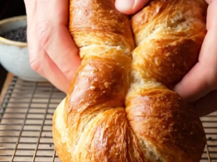 Golden twisted Turkish açma bagels on a parchment-lined baking sheet, glossy with egg wash and sprinkled with nigella seeds