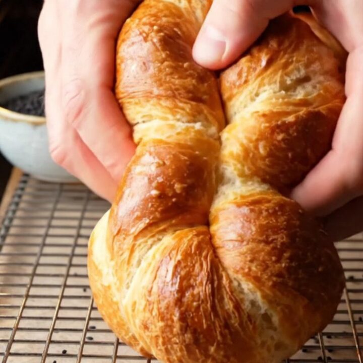 Golden twisted Turkish açma bagels on a parchment-lined baking sheet, glossy with egg wash and sprinkled with nigella seeds
