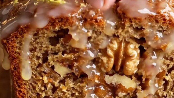 Sliced whole-lemon walnut loaf cake with a glossy white glaze and lemon zest curls on top